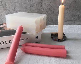 May include: A clear silicone mold for making candles, with six round cavities.  Three pink candles and a white candle are shown next to the mold.  The white candle is lit.