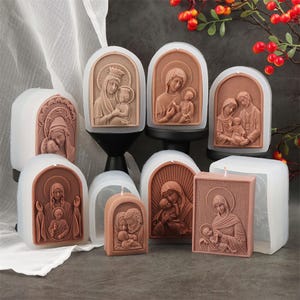 May include: A collection of silicone molds for candle making, featuring various embossed religious scenes of a parent and child. The molds are translucent white with terracotta-colored wax inserts showing detailed figures in arched frames.
