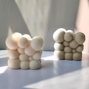 Könnte beinhalten: Zwei dekorative Seifen-Skulpturen in Form einer Blasenansammlung. Eine ist weiß und die andere ist grau.