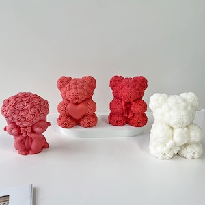 May include: Three rose bear figurines. Two are red and one is white. The red bears are holding a heart and a bow. The white bear is holding a rose.