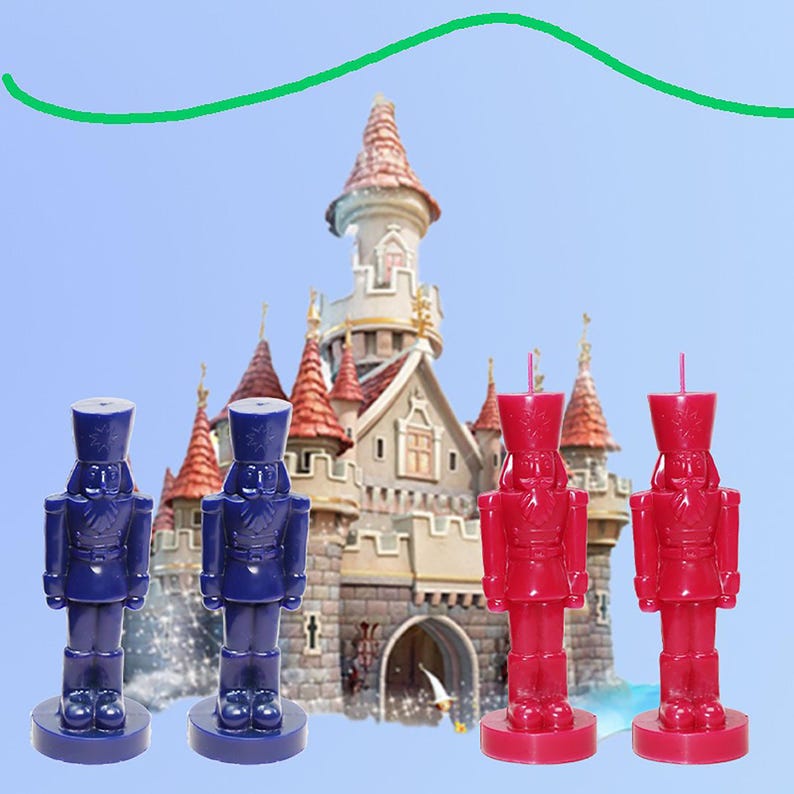 May include: Four nutcracker-shaped candles in the image. Two are navy blue, and two are red. The candles are in front of a castle with a blue sky background. The candles are standing on a round base.