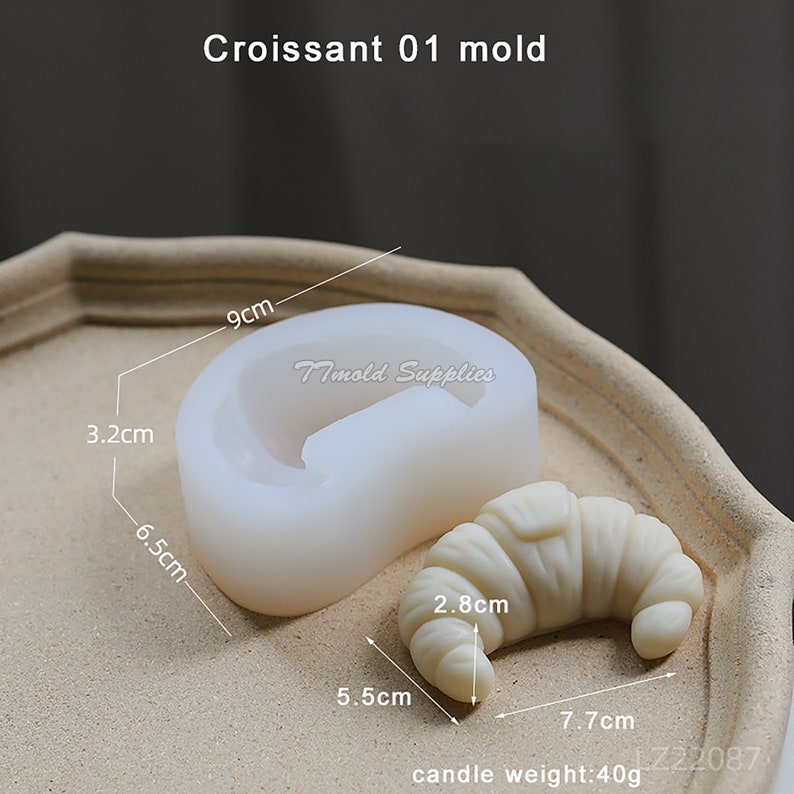 Puede incluir: Molde de silicona blanco con forma de croissant, que mide 9 cm de ancho, 6,5 cm de alto y 3,2 cm de profundidad. Se muestra una vela de croissant de muestra junto al molde, que mide 7,7 cm de largo, 5,5 cm de ancho y 2,8 cm de alto. La vela pesa 40 gramos.