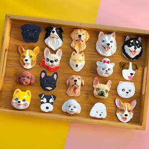 Puede incluir: Una colección de 20 figuritas de diferentes razas de perros, cada una con características y colores únicos. Las figuritas están hechas de un material liso y blanco y están dispuestas en una bandeja de madera.