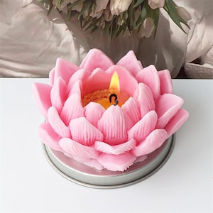 May include: A pink lotus flower candle with a lit wick in the center. The candle is in a silver metal container.