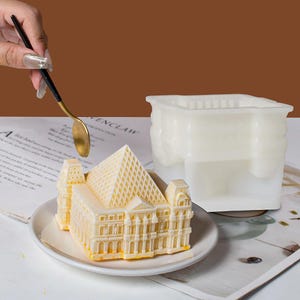 Puede incluir: Un molde de silicona blanco con forma de edificio con techo de pirámide. Un pastel blanco decorado con un diseño similar está sentado en un plato blanco.