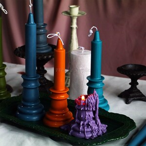 May include: Assortment of colorful candles in various sizes and shapes, including teal, orange, purple, and white. The candles are displayed on a green tray with a black metal candlestick.