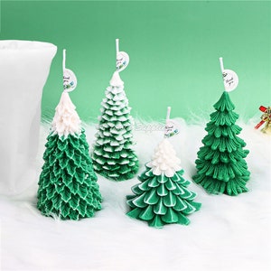 Puede incluir: Cuatro velas de árbol de Navidad verdes y blancas con una etiqueta blanca que dice "Gracias" en cada una. Las velas están sobre una superficie blanca y esponjosa.