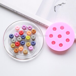 May include: A pink silicone mold with nine round cavities for making small, round candies or decorations. A clear plate holds a variety of colorful candies made with the mold.