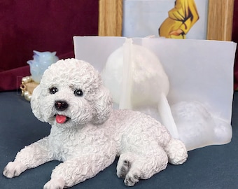 May include: White ceramic figurine of a small dog lying down. The dog has a fluffy white coat and a pink tongue sticking out. The figurine is on a gray surface.