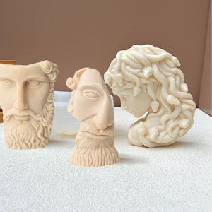 Könnte beinhalten: Drei Gips-Skulpturen von menschlichen Köpfen. Die Skulpturen sind in einem neutralen Beige gehalten. Eine Skulptur ist die eines Mannes mit Bart, eine andere die einer Frau mit Schlangen im Haar und die dritte die eines Mannes mit Bart und einer großen Nase.