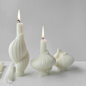 May include: Three white, decorative candles with a unique, organic, and textured design. The candles are lit and have a warm, inviting glow.