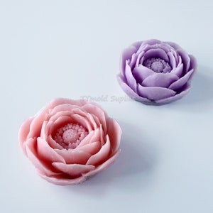 May include: Two handmade soap flowers, one pink and one purple, with detailed petal designs. The flowers are made to look like real roses.