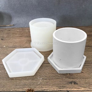 May include: Two white silicone molds for making concrete planters. The molds are in the shape of a cylinder and a hexagon. The molds are on a wooden surface.