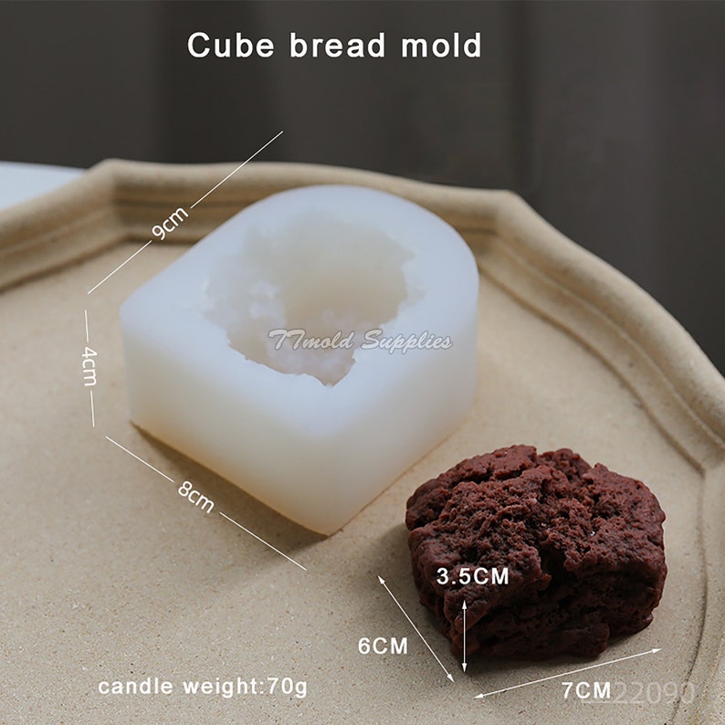 Puede incluir: Molde de silicona blanco para hacer pan en forma de cubo. El molde mide 9 cm de largo, 8 cm de ancho y 4 cm de alto. Se muestra una hogaza de pan en forma de cubo marr&oacute;n junto al molde. La hogaza de pan mide 6 cm de largo, 7 cm de ancho y 3,5 cm de alto. El texto "Imold Supplies" est&aacute; impreso en el molde. El texto "peso de la vela: 70 g" est&aacute; impreso debajo del molde.