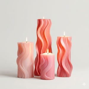 May include: Four pillar candles in shades of pink and coral, featuring a wavy, textured design. Each candle has a lit wick, producing a warm glow. The candles are arranged against a white backdrop.