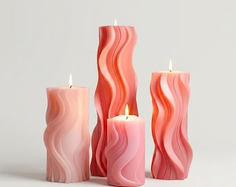 May include: Four pillar candles in varying shades of pink and coral, with a wavy, textured design. Each candle has a lit wick, creating a warm glow. The candles are arranged on a white background.
