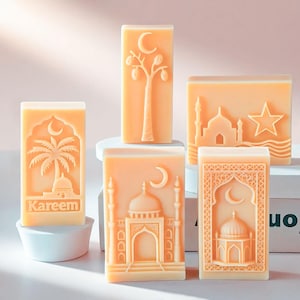 May include: Five rectangular, light orange soaps with intricate designs. The soaps feature images of a mosque, a palm tree, a tree with fruit, a star, and a crescent moon. One soap has the word "Kareem" engraved.