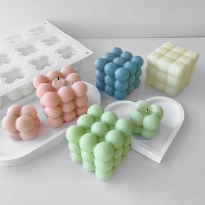 May include: Five colourful bubble-shaped candles in various colours, including pink, blue, green, and yellow. The candles are arranged on a white surface with a white silicone mould in the background.