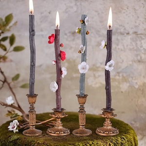 Puede incluir: Cuatro candelabros decorativos con velas grises y moradas. Las velas están decoradas con flores blancas y rosas. Los candelabros son de metal dorado.