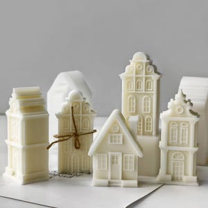 May include: Set of six white miniature houses with intricate details, including windows, doors, and roofs. The houses are made of a smooth, white material and are arranged on a white surface.