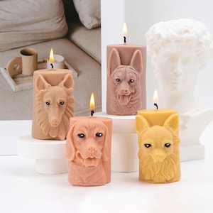 May include: Set of five pillar candles with dog faces. The candles are in shades of brown and yellow, with detailed dog breed faces carved into the wax. Each candle has a lit wick, creating a warm glow.