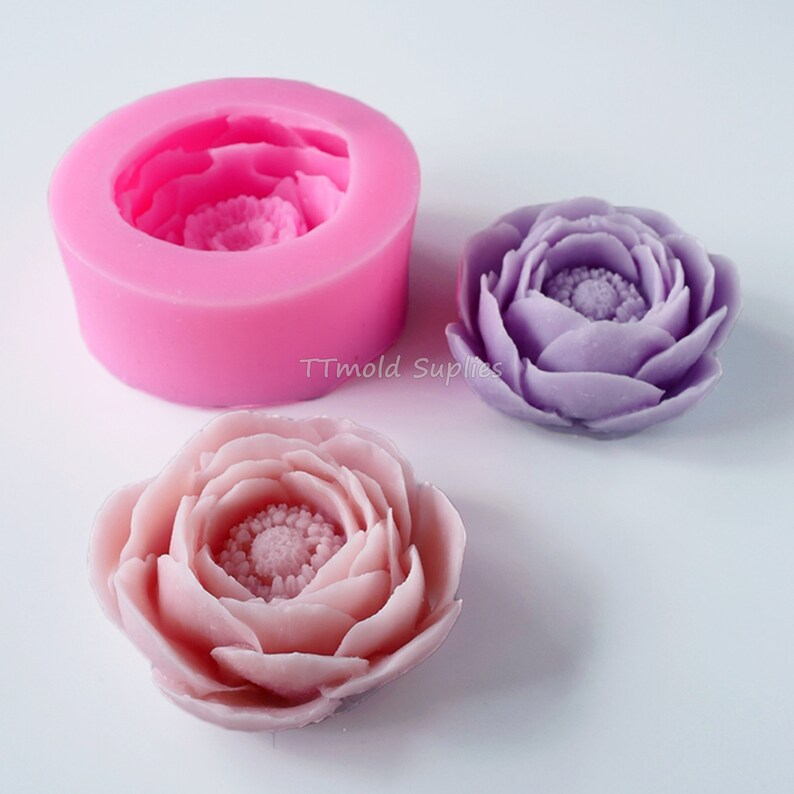 May include: Pink silicone mold for making flower-shaped decorations. Two finished flowers are shown, one in light purple and one in light pink.