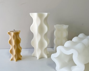 May include: Three candles in different sizes, all with a wavy, textured design. The largest candle is white, the medium candle is white, and the smallest candle is beige.