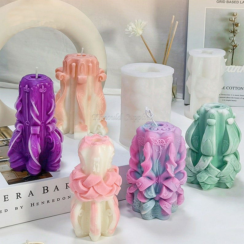 May include: Six different candle molds, including a cylindrical mold, a mold for a candle with a floral design, and a mold for a candle with a more ornate design. The molds are made of white silicone and are shown with finished candles in various colors.