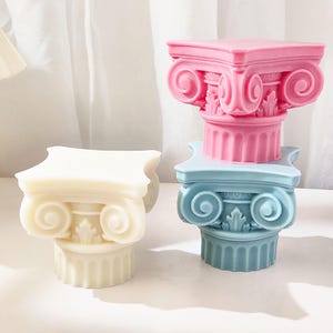 K&ouml;nnte beinhalten: Drei dekorative s&auml;ulenf&ouml;rmige Objekte in Pastellfarben. Eines ist cremefarben, ein anderes hellblau und das dritte rosa. Jedes hat eine quadratische Oberseite und ein detailliertes, klassisches Design. Die Objekte sind wahrscheinlich f&uuml;r die Heimdekoration oder den k&uuml;nstlerischen Gebrauch bestimmt.