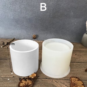 May include: Two white silicone molds for making concrete planters. The molds are 8.5 inches in diameter. The molds are on a wooden surface.