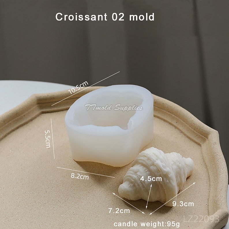 Puede incluir: Un molde de silicona blanco con forma de croissant, que mide 8,2 cm de ancho, 5,5 cm de alto y 10,5 cm de largo. Junto al molde hay una vela blanca con forma de croissant, que mide 7,2 cm de largo, 4,5 cm de ancho y 9,3 cm de alto. La vela pesa 95 gramos. El texto "Timold Supplies" y "LZ22093" es visible en la imagen.