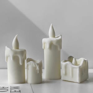 May include: Four white wax candles with a drip effect. The candles are different sizes and shapes.
