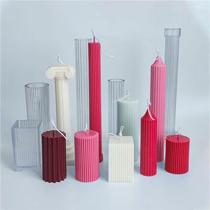 Könnte beinhalten: Eine Auswahl an Säulenkerzen in verschiedenen Farben und Formen. Die Kerzen umfassen eine weiße Säule, eine quadratische Kerze und mehrere zylindrische Kerzen in Rot-, Rosa- und Grüntönen. Klare Kunststoffformen sind ebenfalls sichtbar.