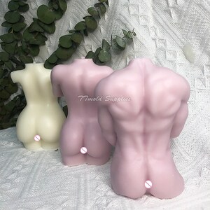 Op de afbeelding: Twee naaktkleurige kaarsen in de vorm van menselijke torso's. De kaarsen zijn gemaakt van een glad, zacht materiaal en hebben een realistisch uiterlijk. De kaarsen staan ​​naast elkaar op een wit oppervlak.