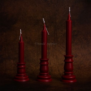 May include: Three red candles of varying heights on matching red candle holders. The candles have white wicks.