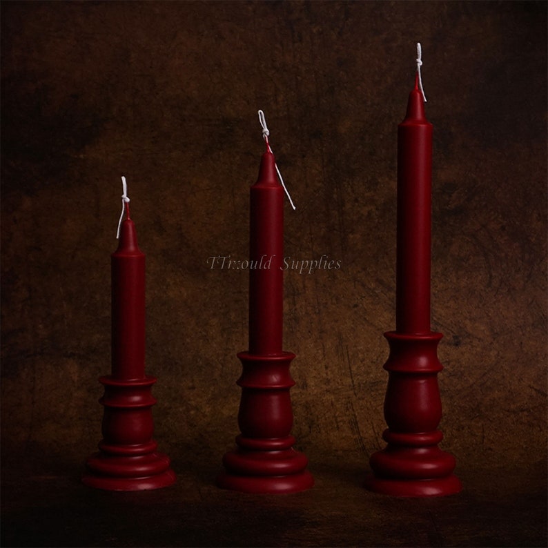 May include: Three red candles of varying heights on matching red candle holders. The candles have white wicks.