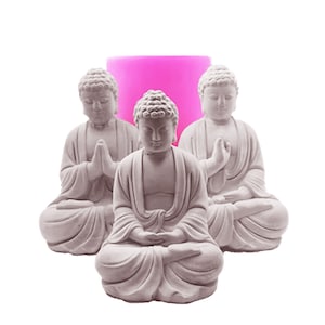 May include: Three gray concrete Buddha statues in a seated meditation pose. The statues are arranged in a semi-circle with a pink silicone mold in the center.