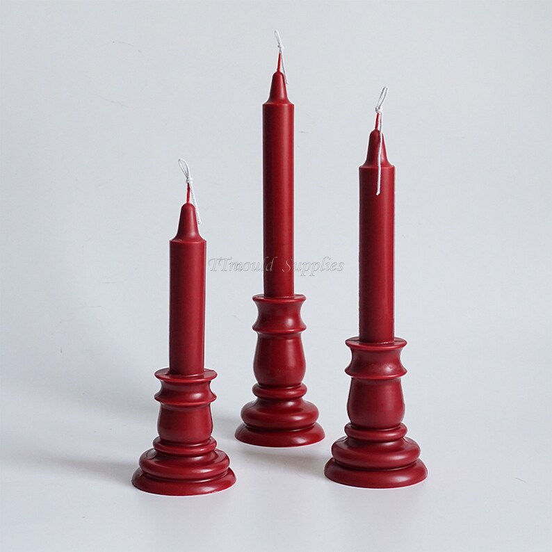May include: Three red candles on wooden candle holders. The candles are tall and thin, with white wicks. The candle holders are a deep red color and have a classic design.