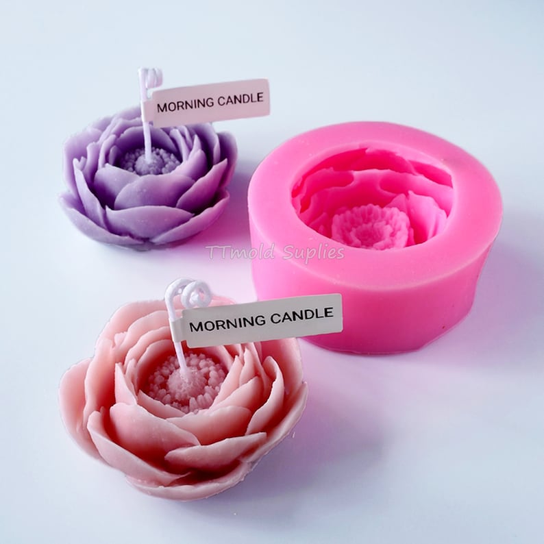 May include: Two pink and purple flower-shaped candles with the text "Morning Candle" on a white label. A pink silicone mold for making the candles is also shown.