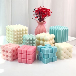 May include: An assortment of geometrically shaped decorative wax melts in various colours, including pink, white, and blue. The wax melts are arranged on a white surface.