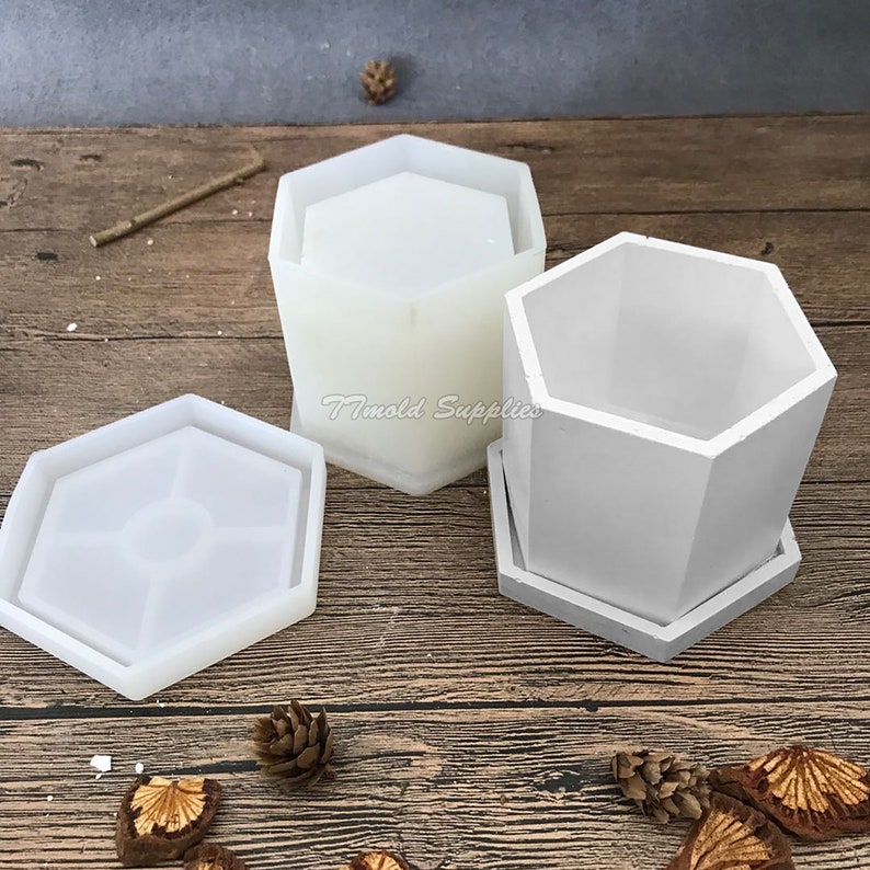 May include: Two white silicone molds for making hexagonal planters. The molds are on a wooden surface with pine cones and other natural elements.