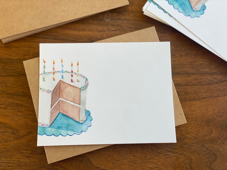 May include: A white card featuring a watercolour illustration of a birthday cake with candles. The cake is brown with white icing and blue sprinkles. The cake is on a blue plate with a scalloped edge.