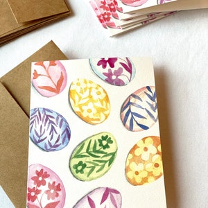 May include: A set of blank greeting cards with a watercolor design of colorful Easter eggs. Each egg is decorated with a different floral pattern.