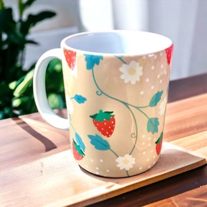 May include: A beige ceramic mug with a white handle features a repeating pattern of red strawberries, white flowers, and green leaves on a beige background.