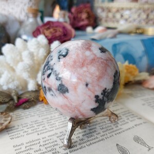 May include: A pink and black marble sphere on a silver stand. The sphere is polished and has a swirling pattern of pink and black.
