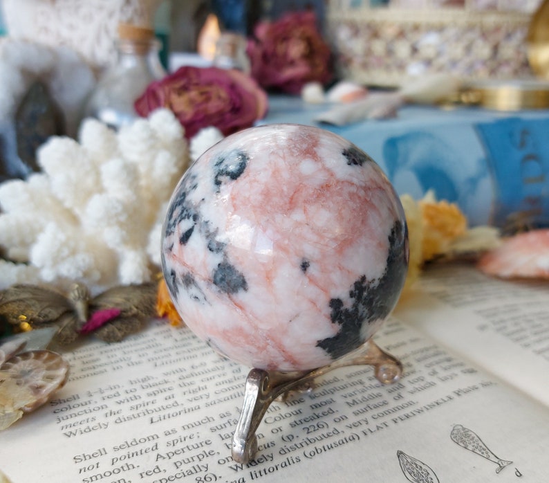 May include: A pink and black marble sphere on a silver stand. The sphere is polished and has a swirling pattern of pink and black.
