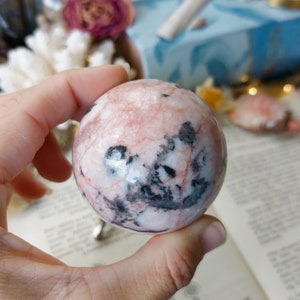 May include: A pink and black sphere of polished stone. The sphere has a swirling pattern of pink and black.