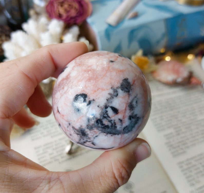 May include: A pink and black sphere of polished stone. The sphere has a swirling pattern of pink and black.