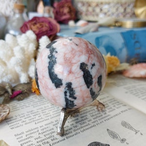 May include: A pink and black striped sphere crystal ball on a metal stand. The sphere is polished and has a smooth surface.