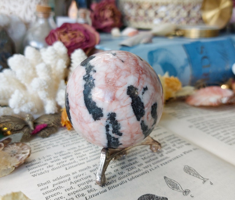 May include: A pink and black striped sphere crystal ball on a metal stand. The sphere is polished and has a smooth surface.